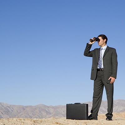 Businessman with briefcase using binoculars in desert